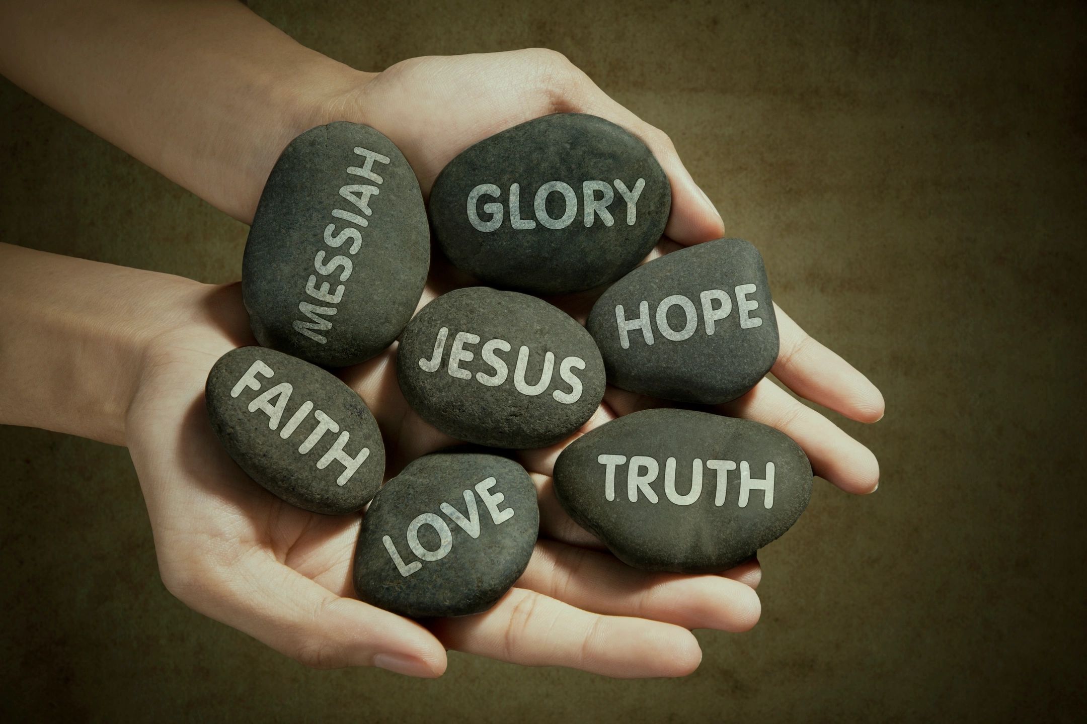 Hands holding engraved stones with words of faith