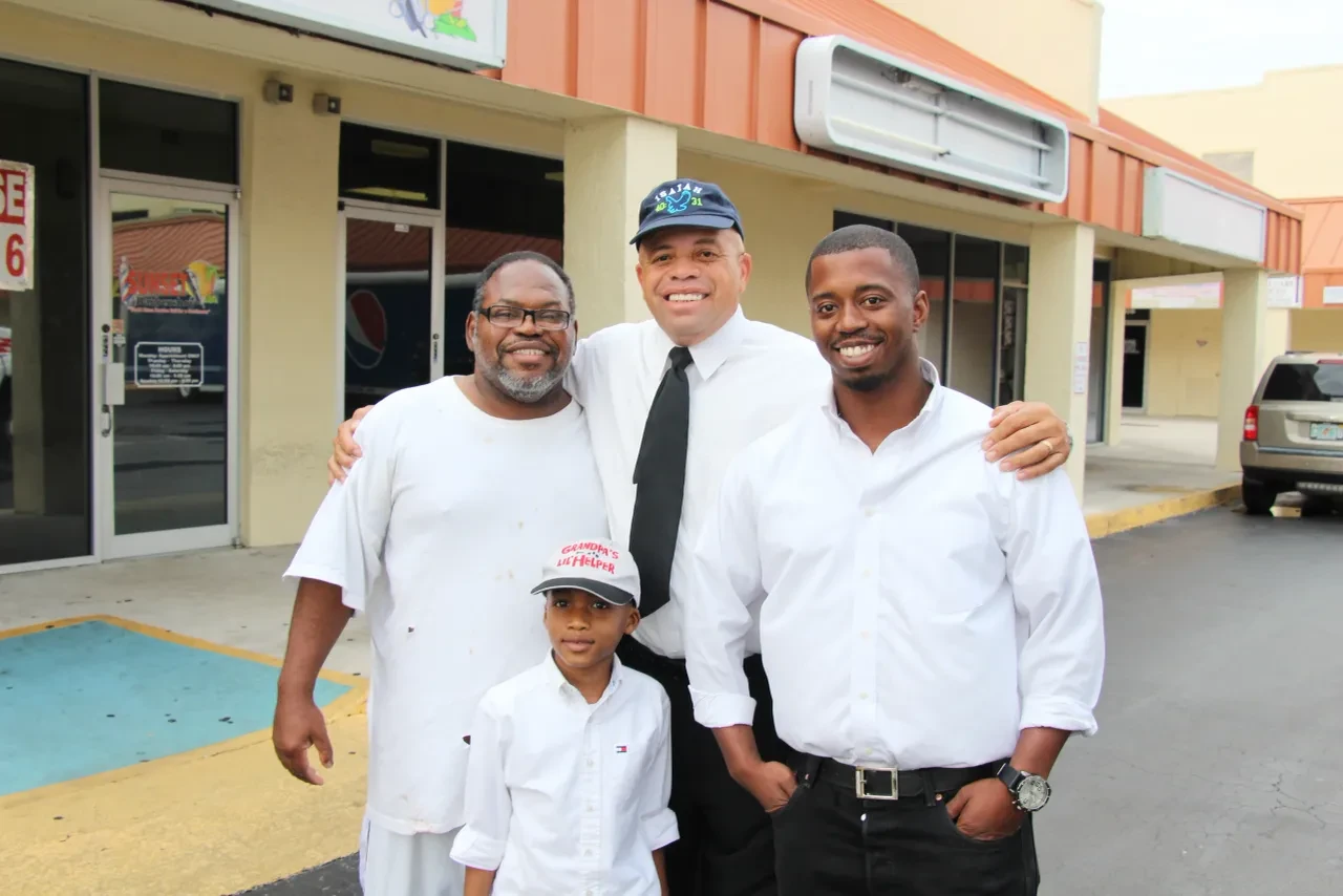 Three men and a child posing outside strip mall at community event