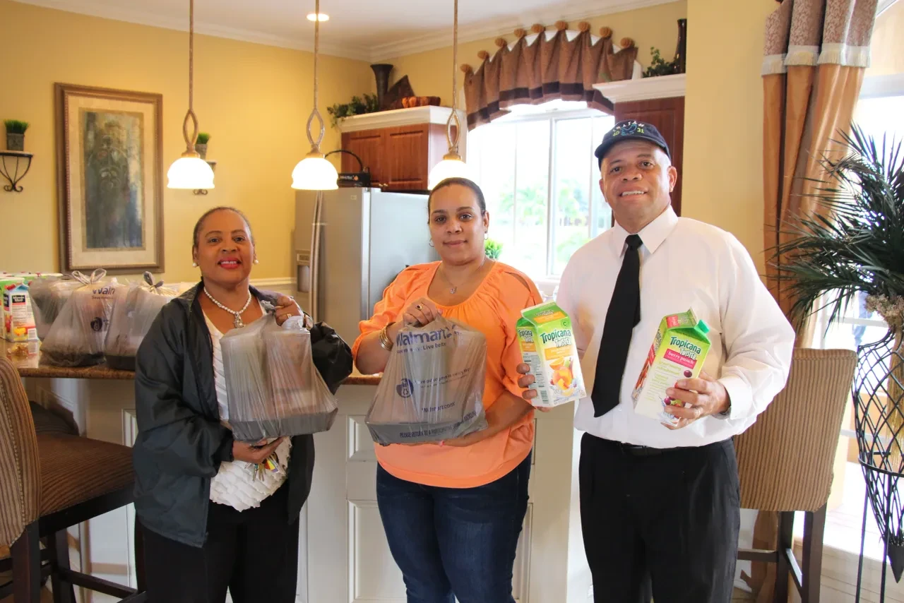 Three volunteers holding grocery bags and juice cartons indoors