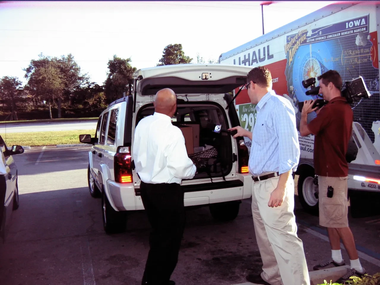 News crew filming volunteer loading SUV next to U-Haul truck