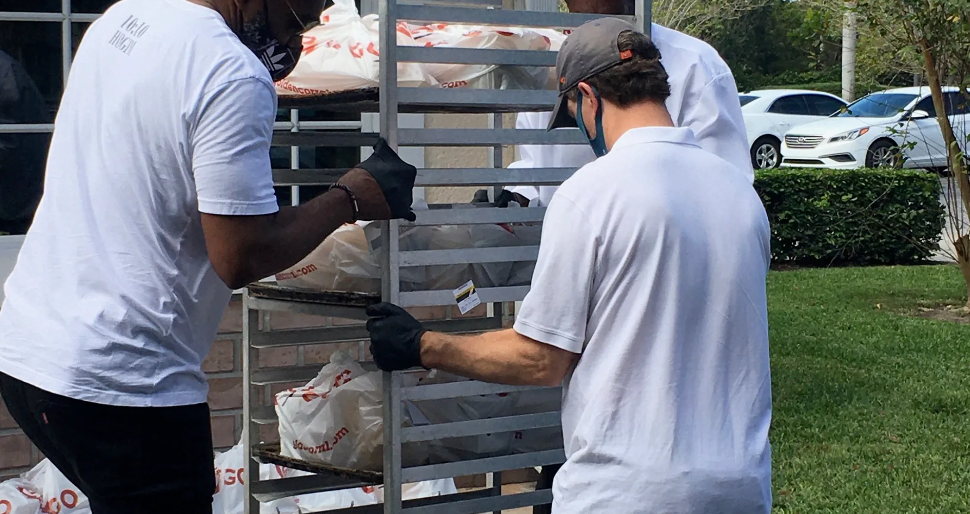Two masked volunteers rolling rack of Golden Corral bags outdoors