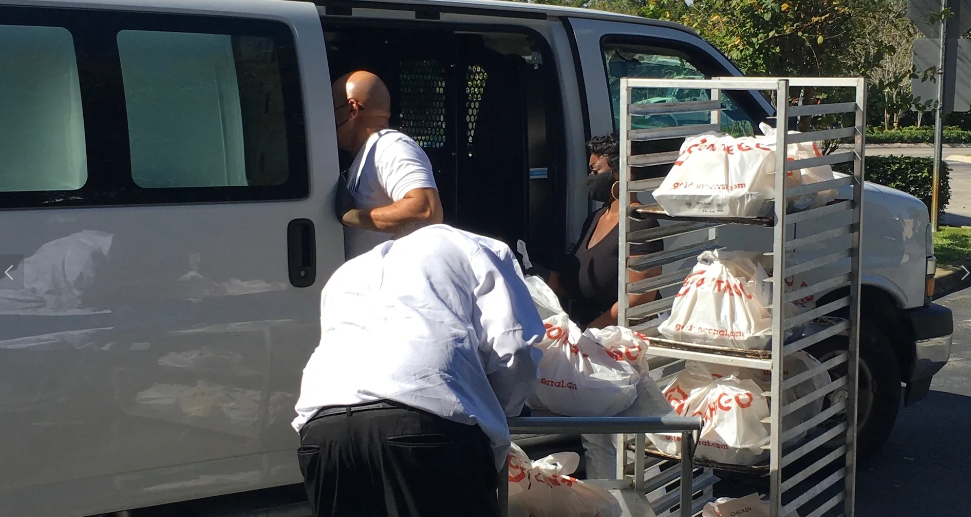 Masked volunteers loading Golden Corral bags from rack into white van