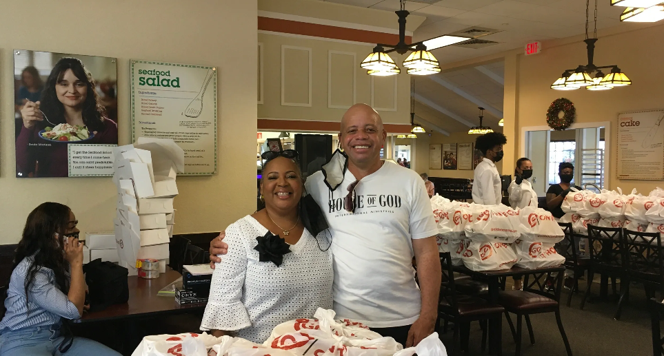 Couple posing at Golden Corral with rows of bagged food donations on tables