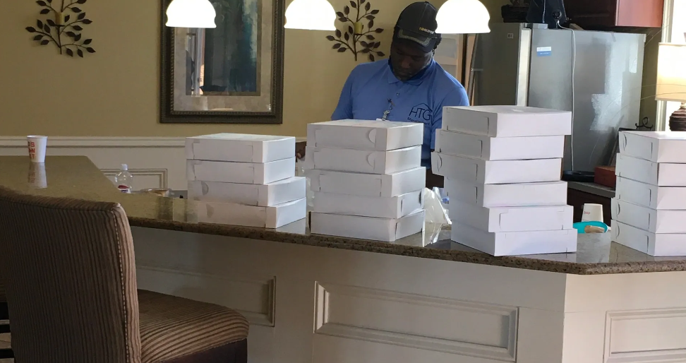 Volunteer in HTG shirt organizing stacked white food boxes on kitchen counter