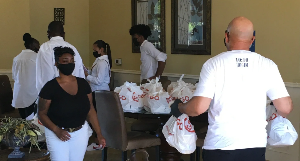 Masked volunteers in white shirts sorting Golden Corral food bags indoors