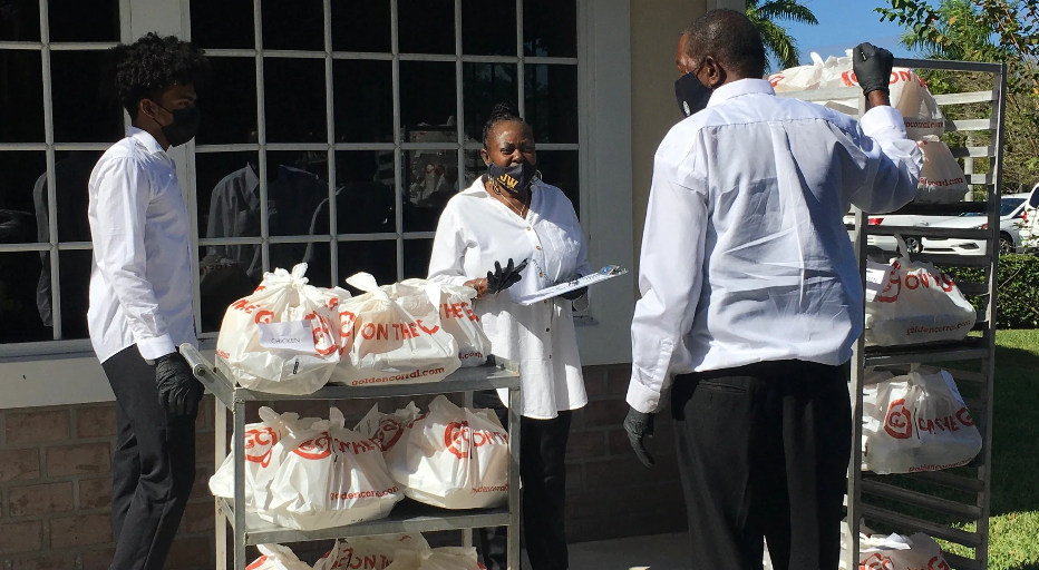 Three masked volunteers loading Golden Corral bags onto outdoor cart