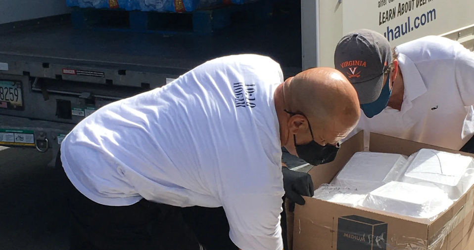 Two masked volunteers unloading foam food containers from U-Haul truck outdoors