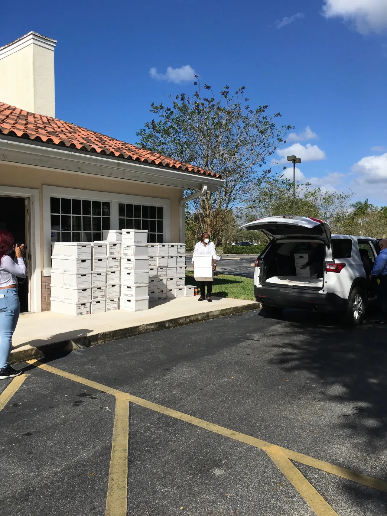 Volunteer carrying box outside building with SUV and stacked boxes