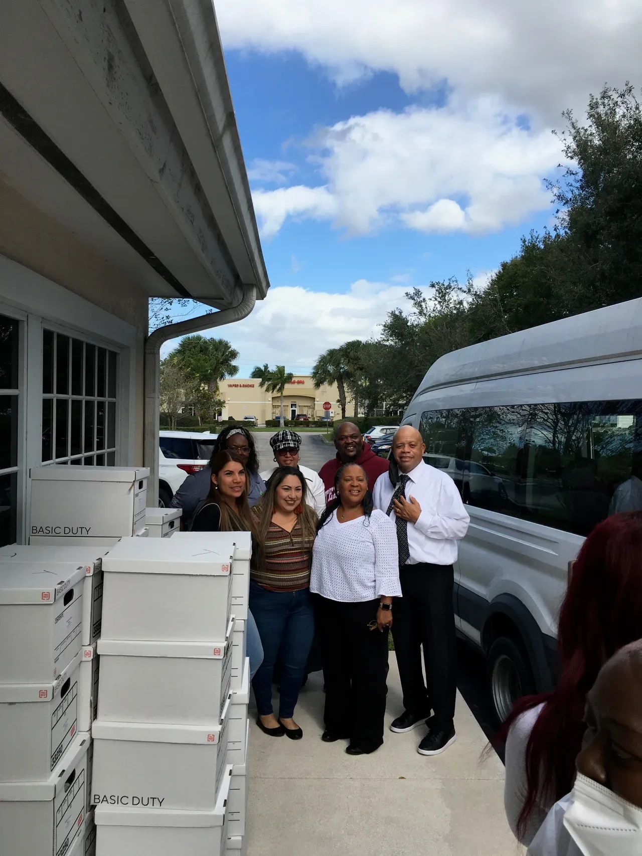 Group of volunteers posing outside with van and stacked boxes