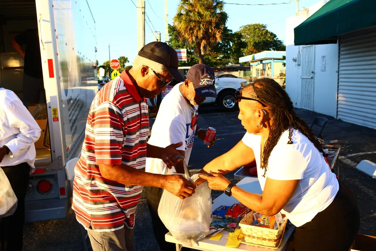 Volunteer handing grocery bag to community member at outdoor distribution table