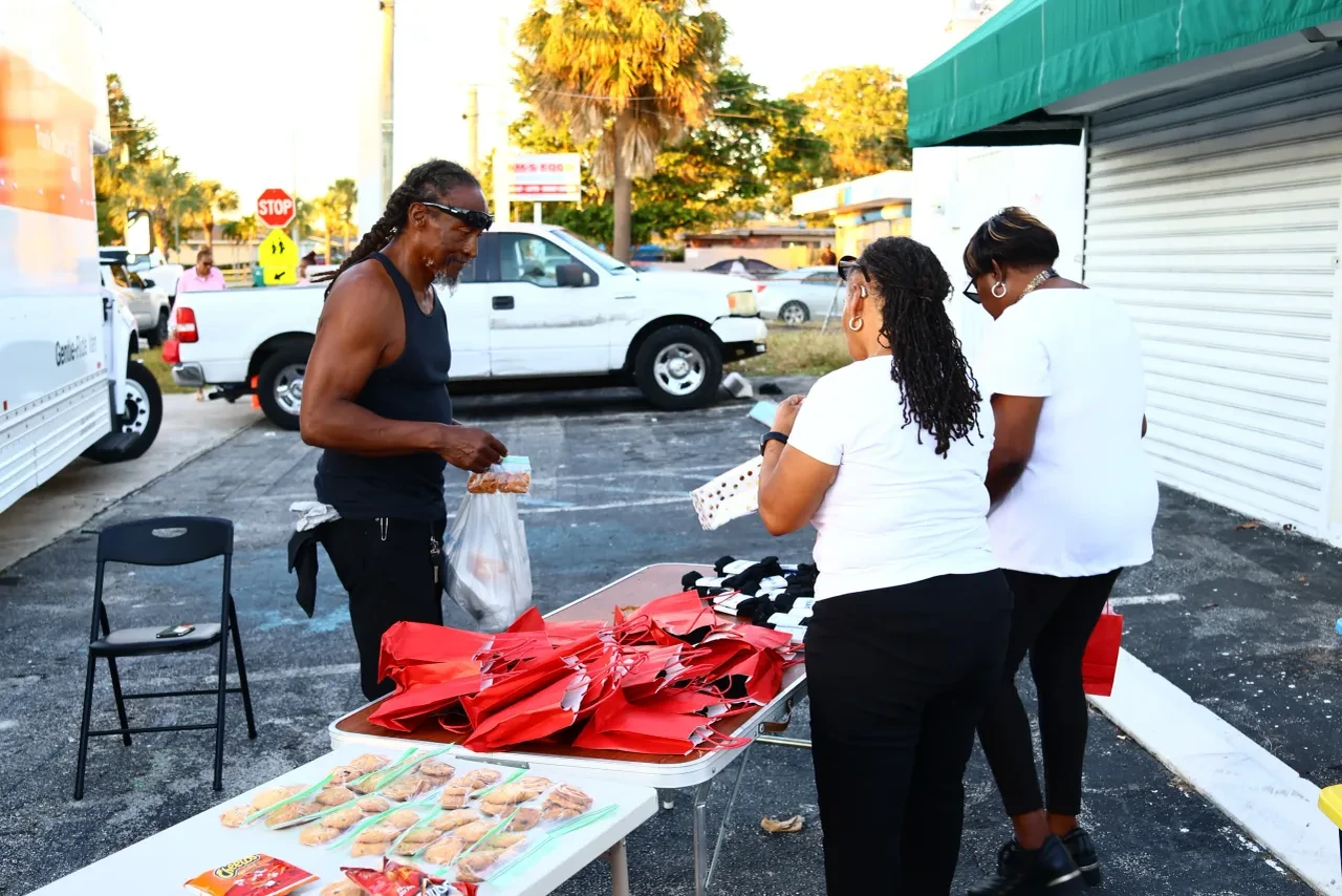 Man receiving red gift bags and food from two volunteers at outdoor table
