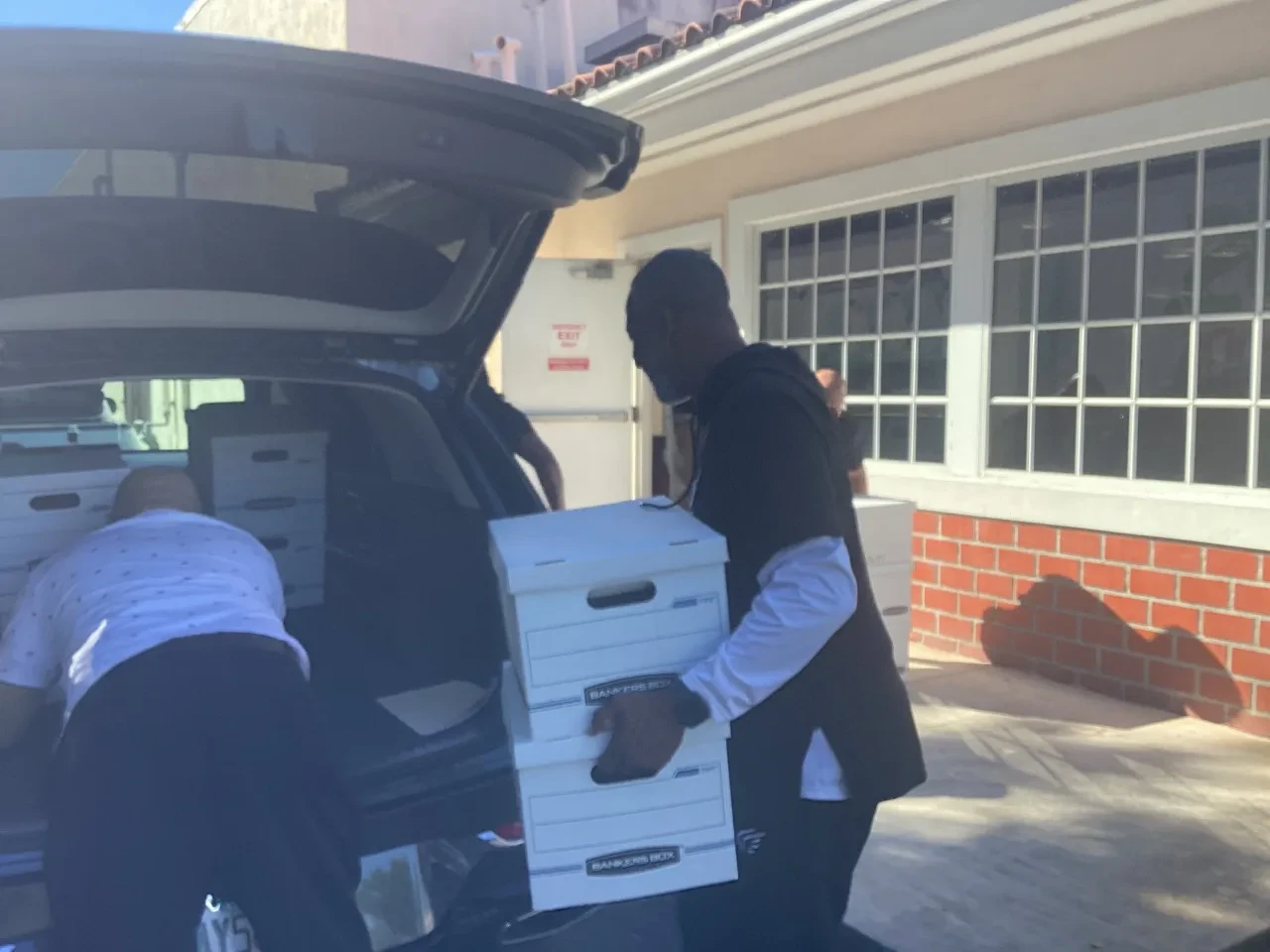 Two volunteers loading Bankers Boxes into SUV at community distribution