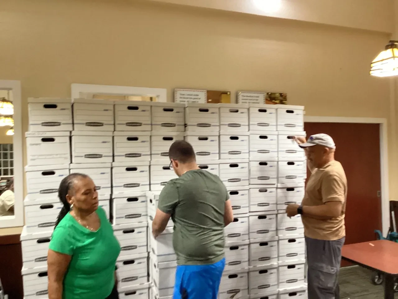 Three volunteers stacking large wall of white Bankers Boxes indoors
