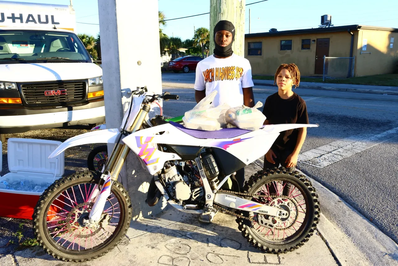 Two young men posing with customized dirt bike at U-Haul community event