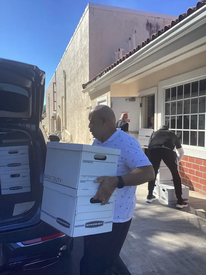 Volunteer carrying stacked Bankers Boxes from vehicle at outdoor distribution