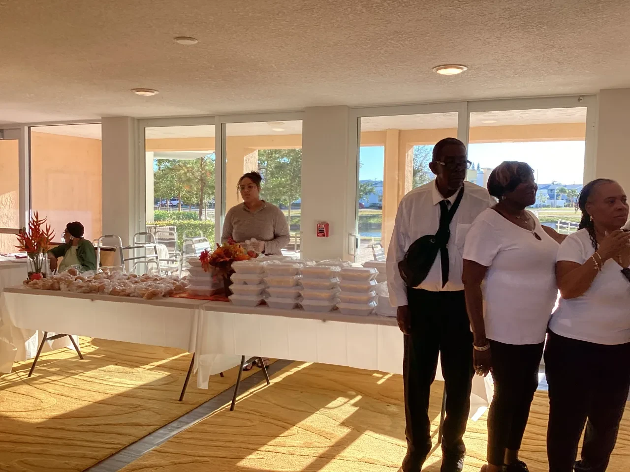 Volunteers and community members at indoor food distribution table with waterfront view