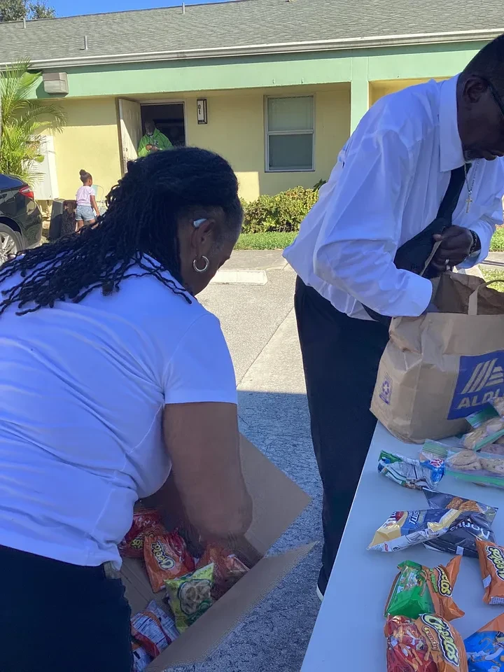 Two volunteers packing Aldi grocery bags with snacks at outdoor table