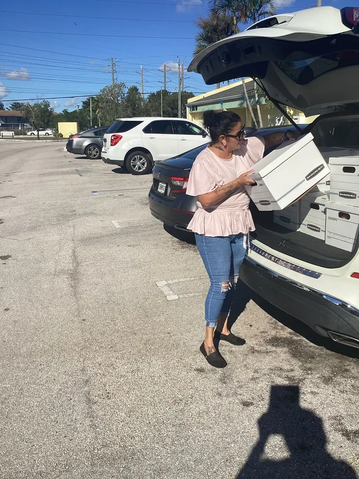 Woman unloading Bankers Boxes from SUV trunk in sunny parking lot