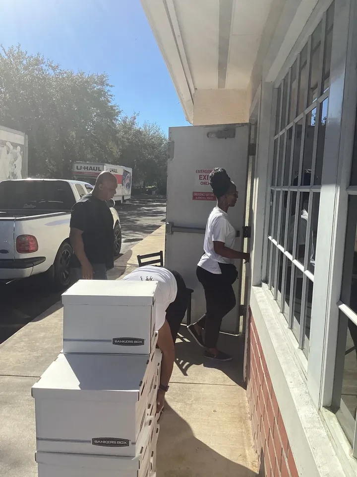 Volunteers carrying Bankers Boxes through emergency exit door with U-Haul truck in background