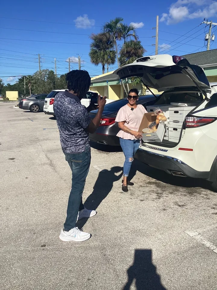Volunteer being photographed while unloading food boxes from SUV trunk at community event