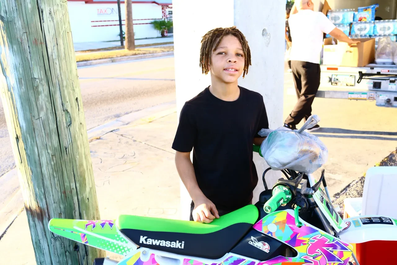 Child smiling beside colorful Kawasaki dirt bike at community event