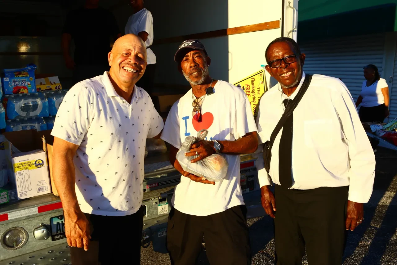 Three men posing together at back of U-Haul truck at Thanksgiving food event