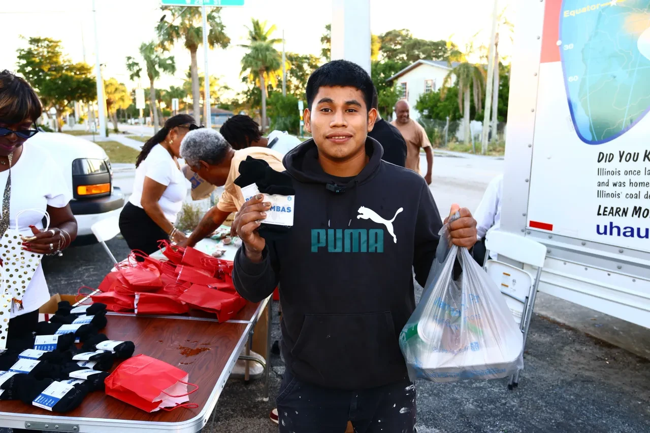 Young man in Puma hoodie smiling while receiving socks and supplies at outdoor distribution table